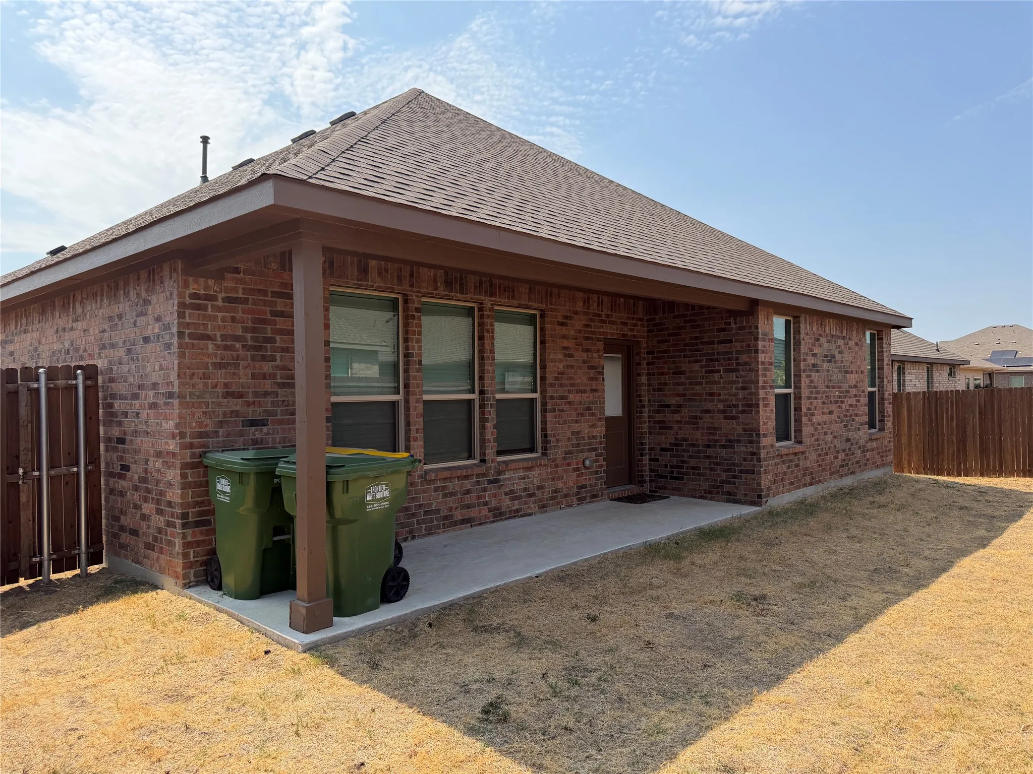 Brick exterior with a covered patio, concrete slab, and wood privacy fencing