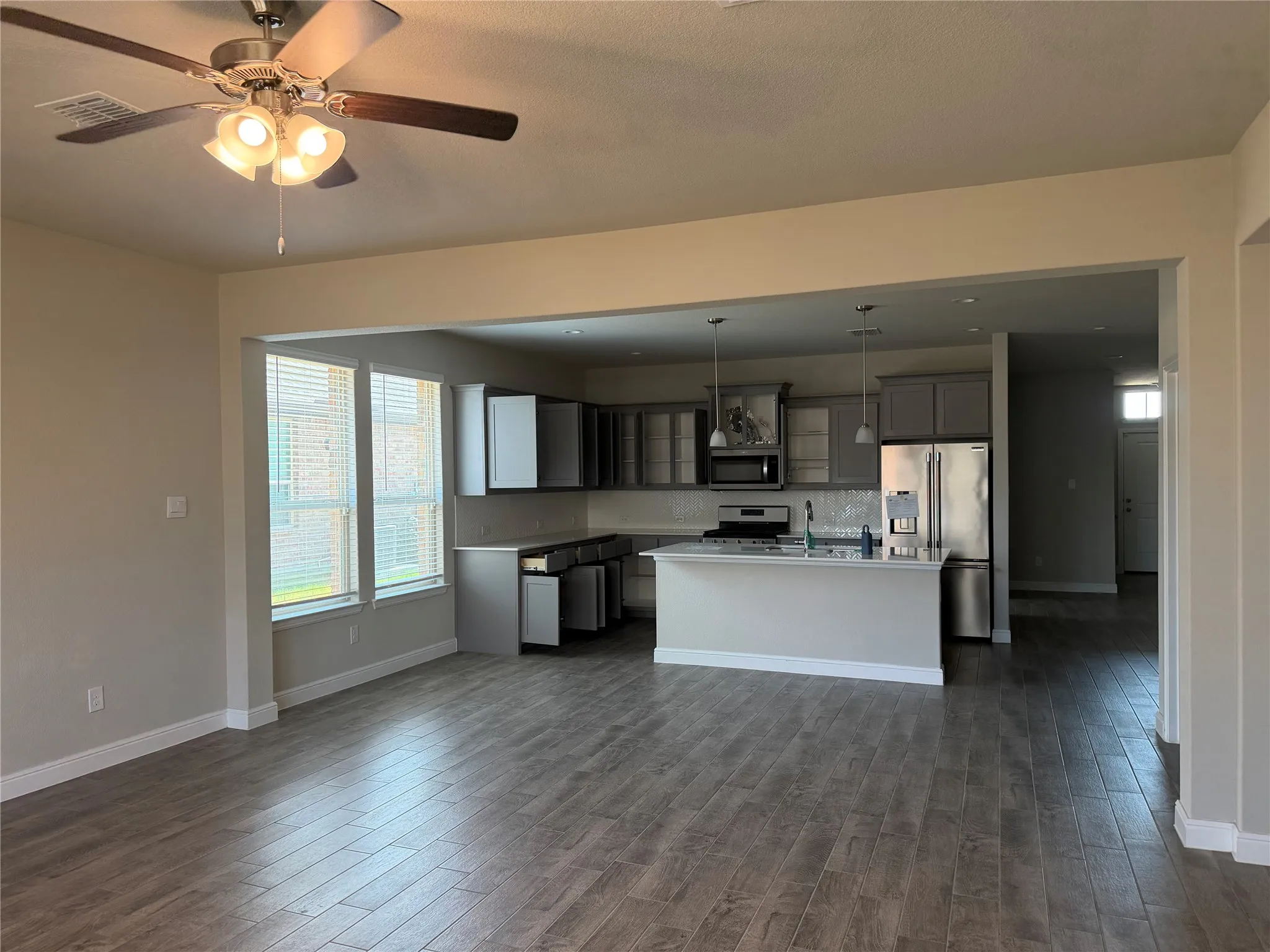 Open-concept living space featuring wood-finish flooring, a ceiling fan, and a kitchen with stainless steel appliances, pendant lighting, and a kitchen island
