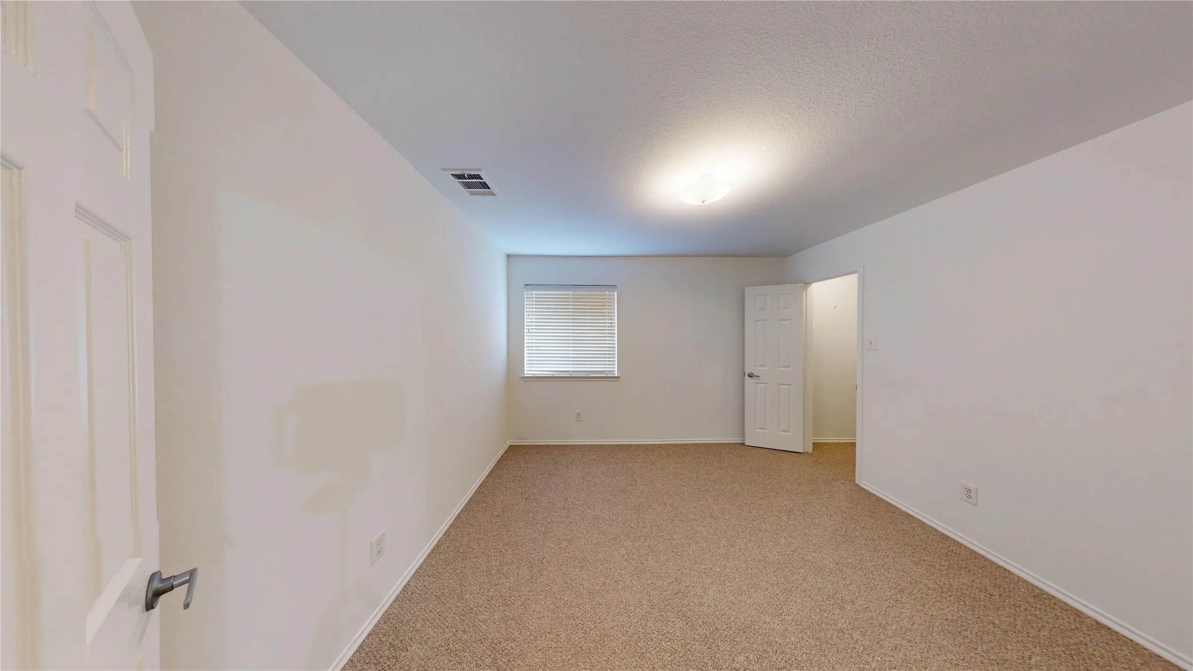 Carpeted flooring, white painted walls, window with blinds, overhead lighting fixture, and a paneled door