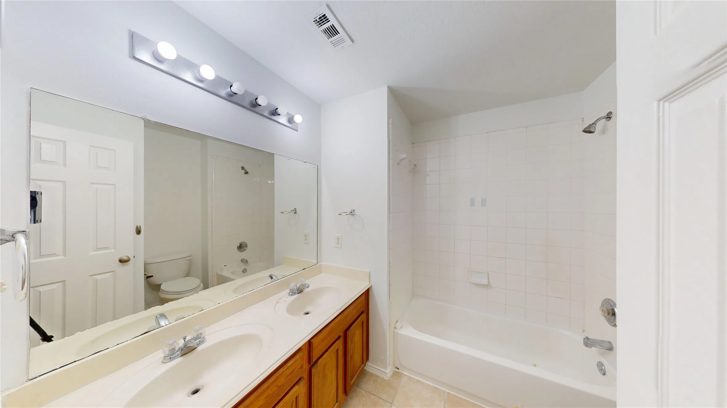 Dual vanity with a laminate countertop, light wood-finish cabinetry, and a full-width wall mirror