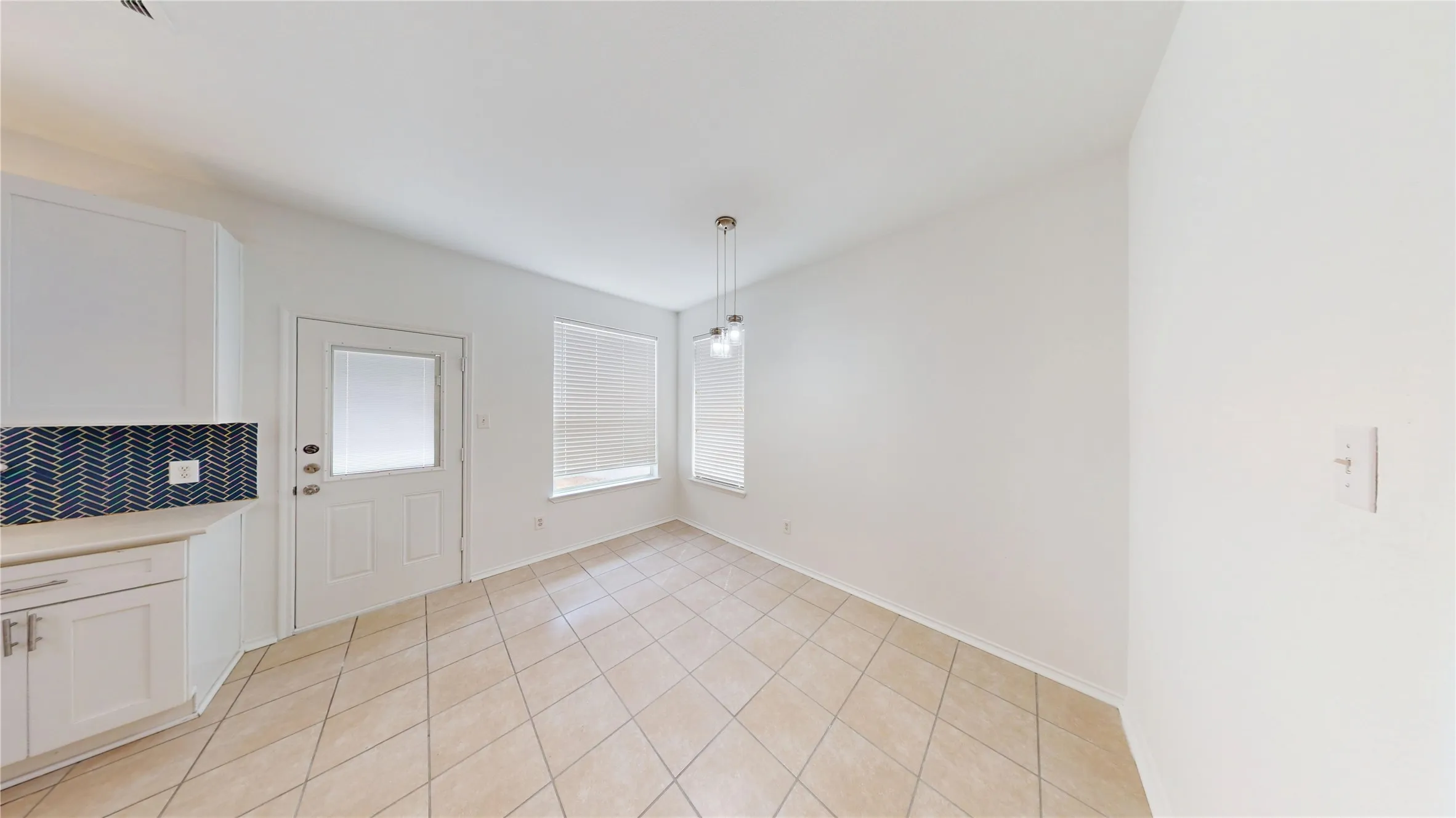 White cabinetry with dark tile backsplash, ceramic tile flooring, two windows with blinds, and pendant lighting