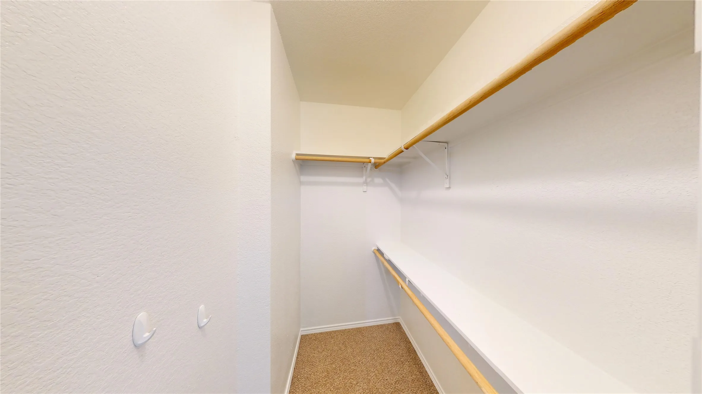 Walk-in closet with carpet flooring, wood-finish hanging rods, and integrated shelving