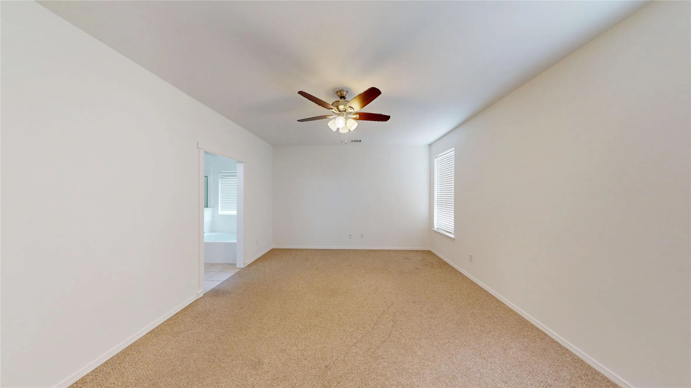 Spacious room with plush carpet flooring, a ceiling fan with integrated lighting, and a window with blinds