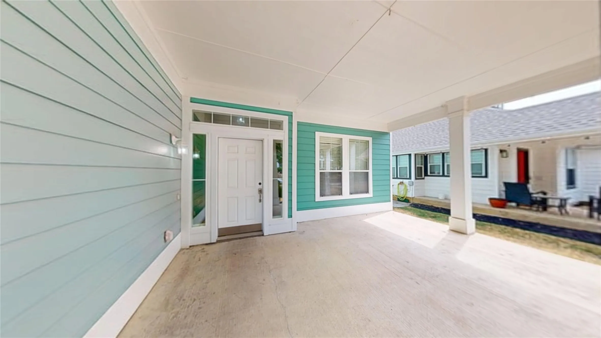 Covered concrete patio with white support columns, light blue siding, and white trim around the front door