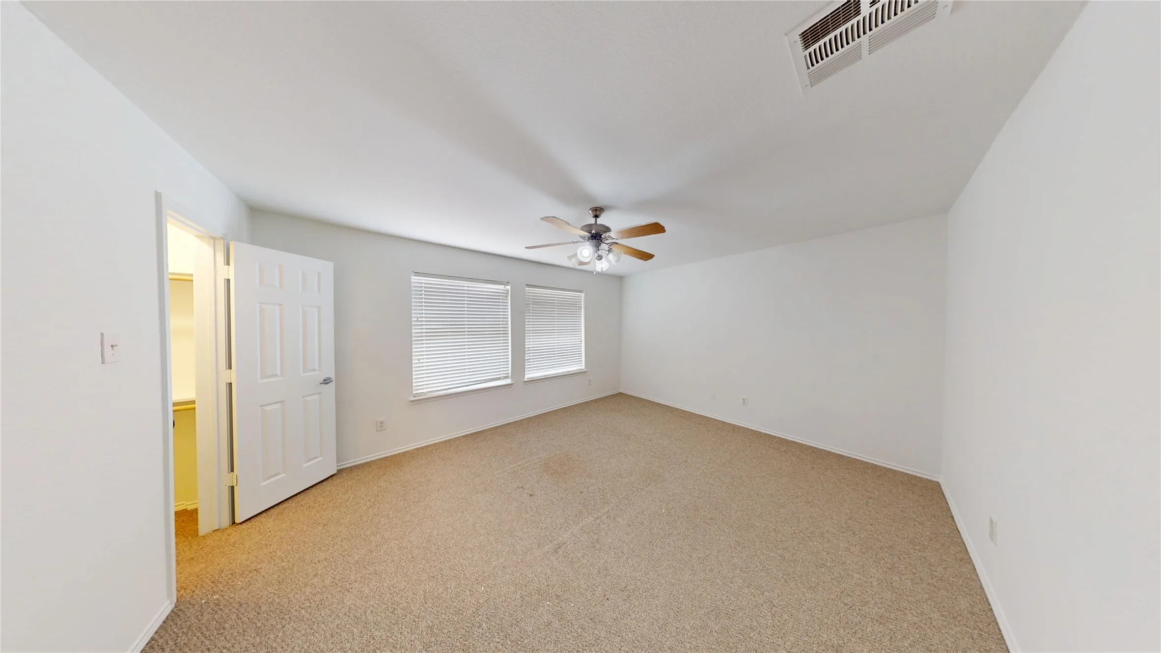Spacious room featuring carpet flooring, two windows with blinds, a ceiling fan, and a built-in closet with shelving