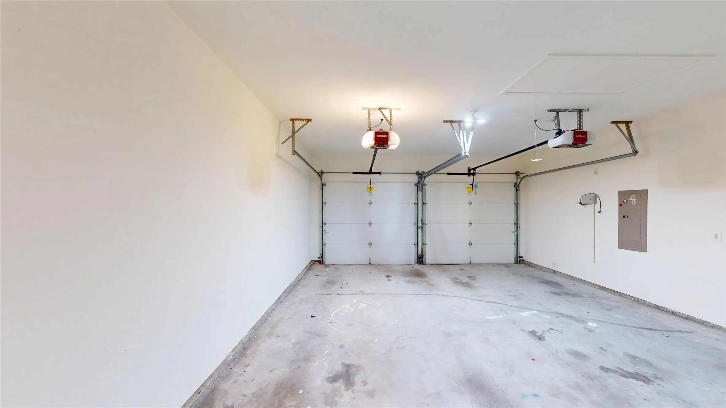 Two-car garage with white paneled garage doors, overhead lighting, and an access panel