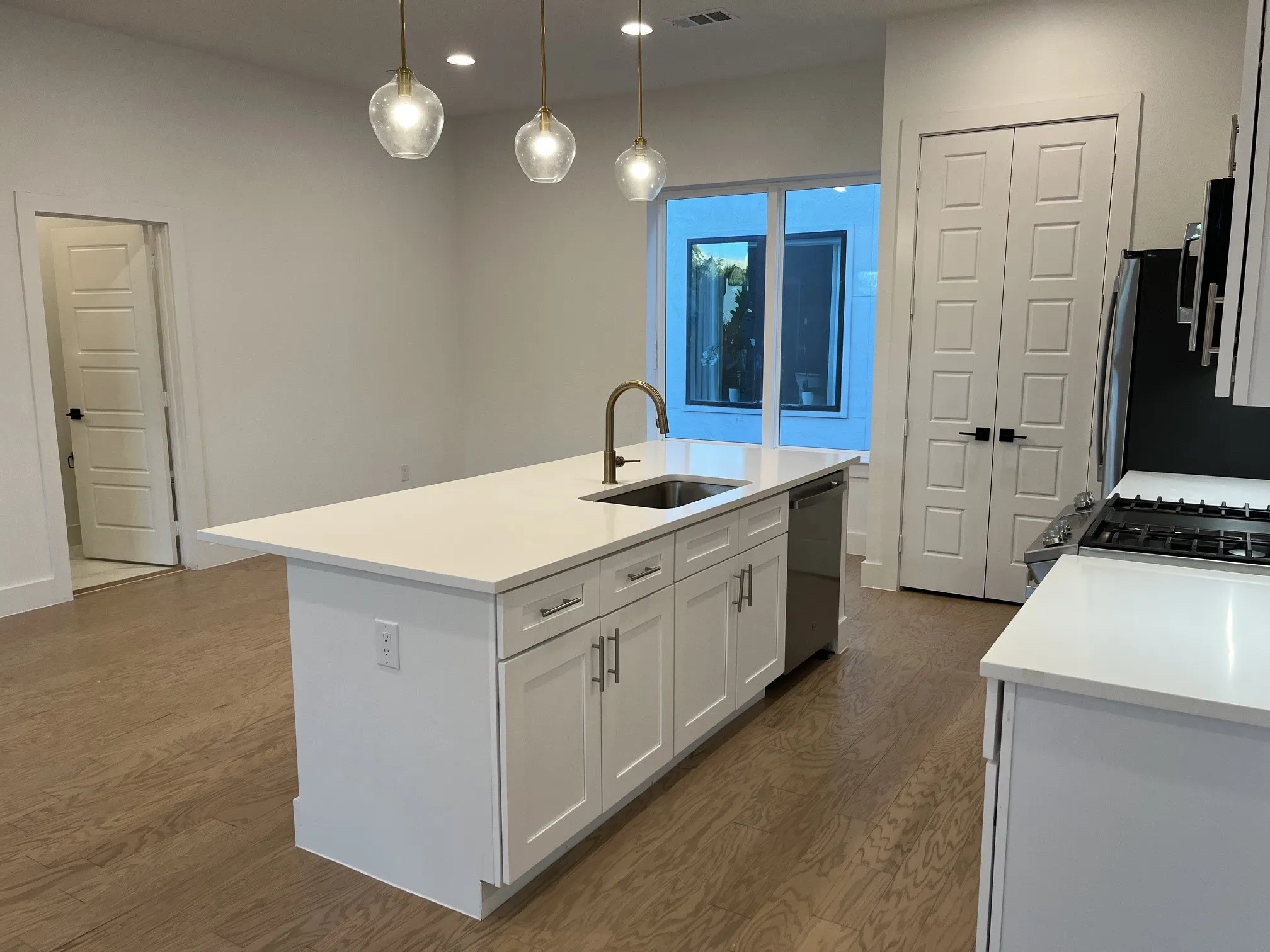 White kitchen island with a built-in sink and gold-finish faucet, recessed lighting, and wood-finish flooring, and a half bath.