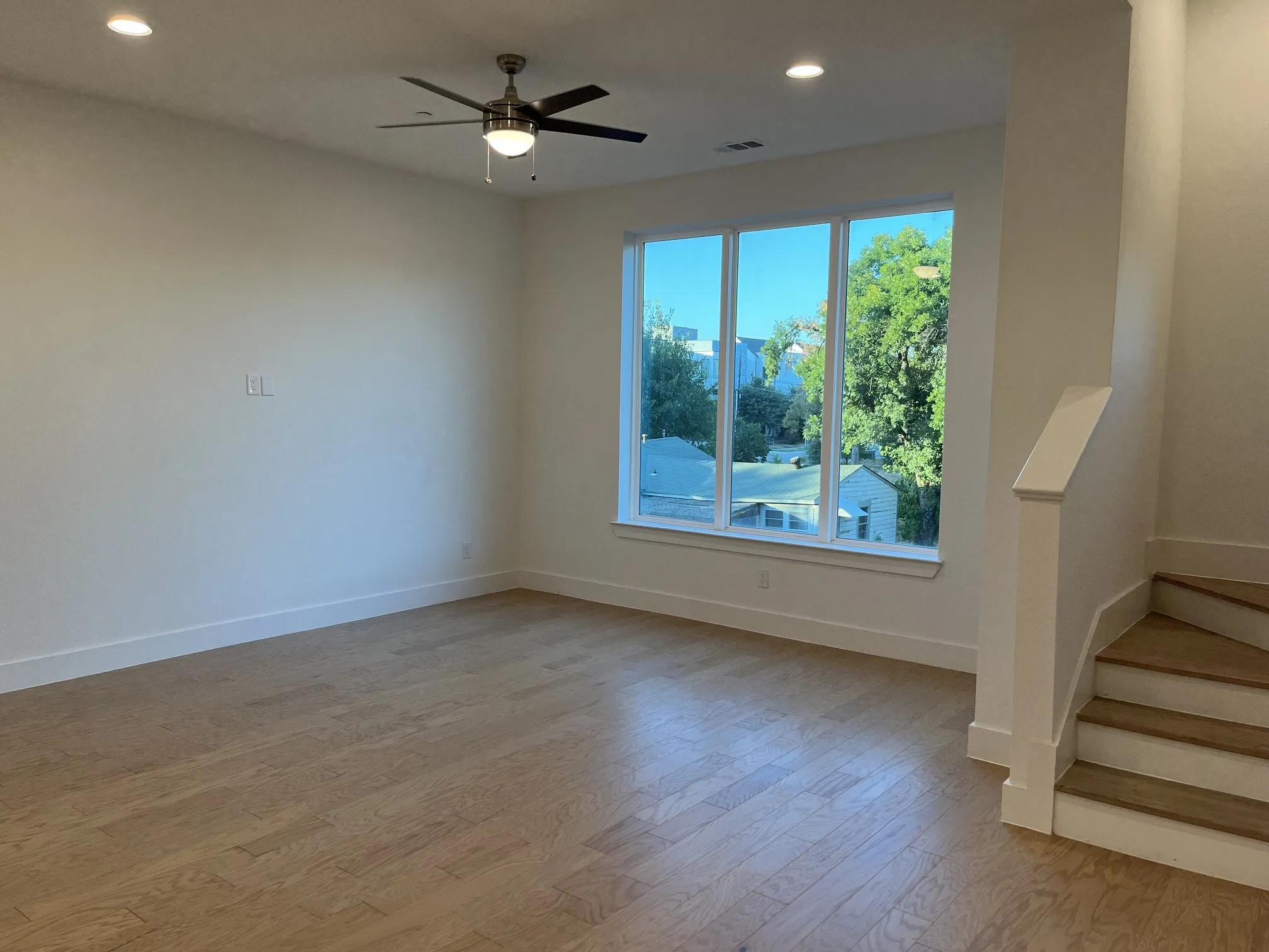 Spacious Living room featuring wood-finish flooring, a contemporary ceiling fan, recessed lighting, expansive windows, and a staircase with wood treads