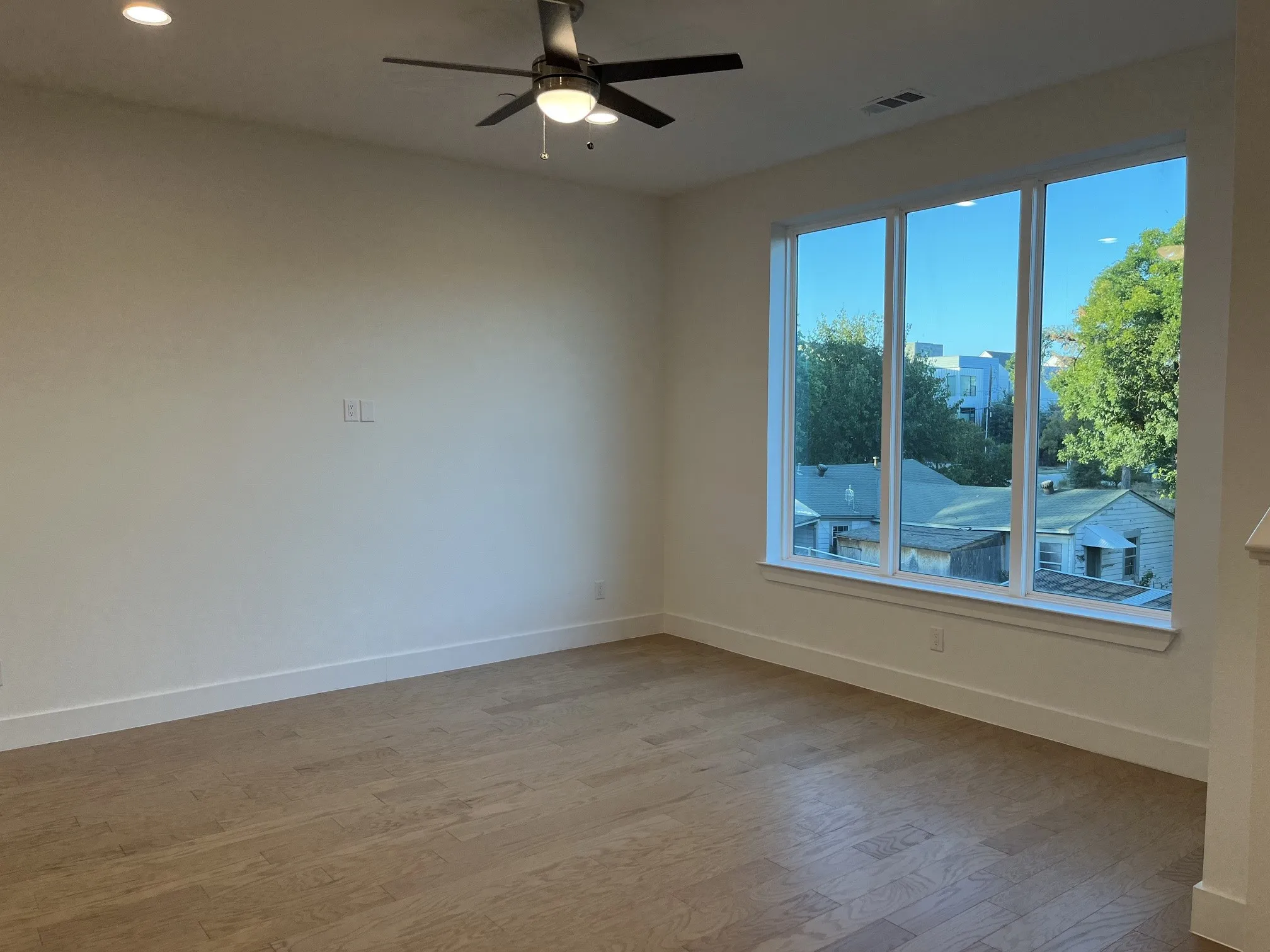 Spacious Living room featuring wood-finish flooring, a large multi-pane window, ceiling fan with integrated lighting, and recessed ceiling lights