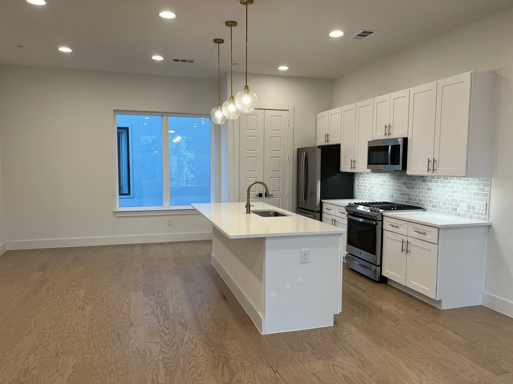 Dining area: Open-concept living space featuring wood-finish flooring, recessed lighting, and a kitchen with white cabinetry, stainless steel appliances, and a tiled backsplash