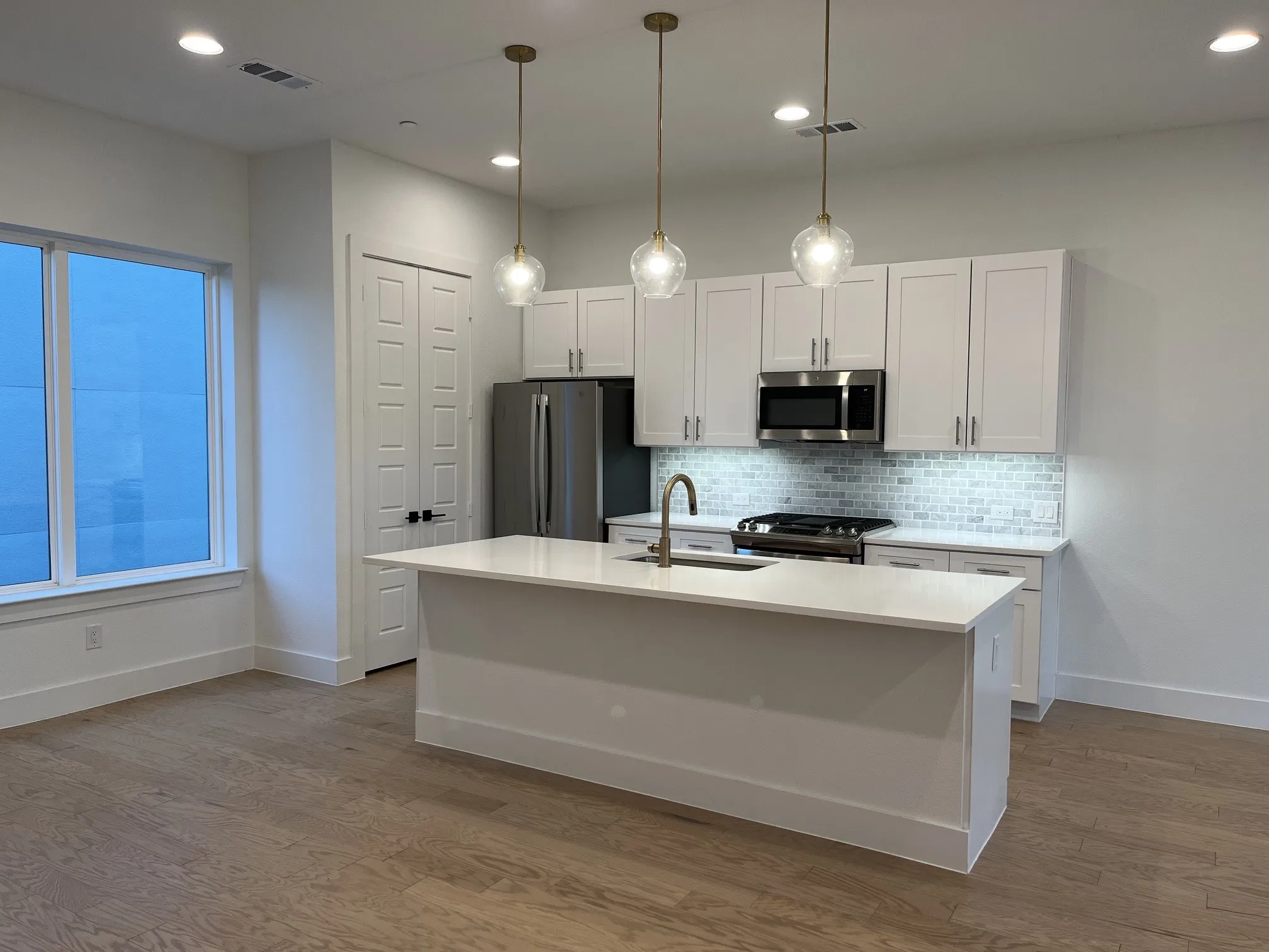 Kitchen featuring white shaker cabinetry, stainless steel appliances, a center island with sink, and pendant lighting