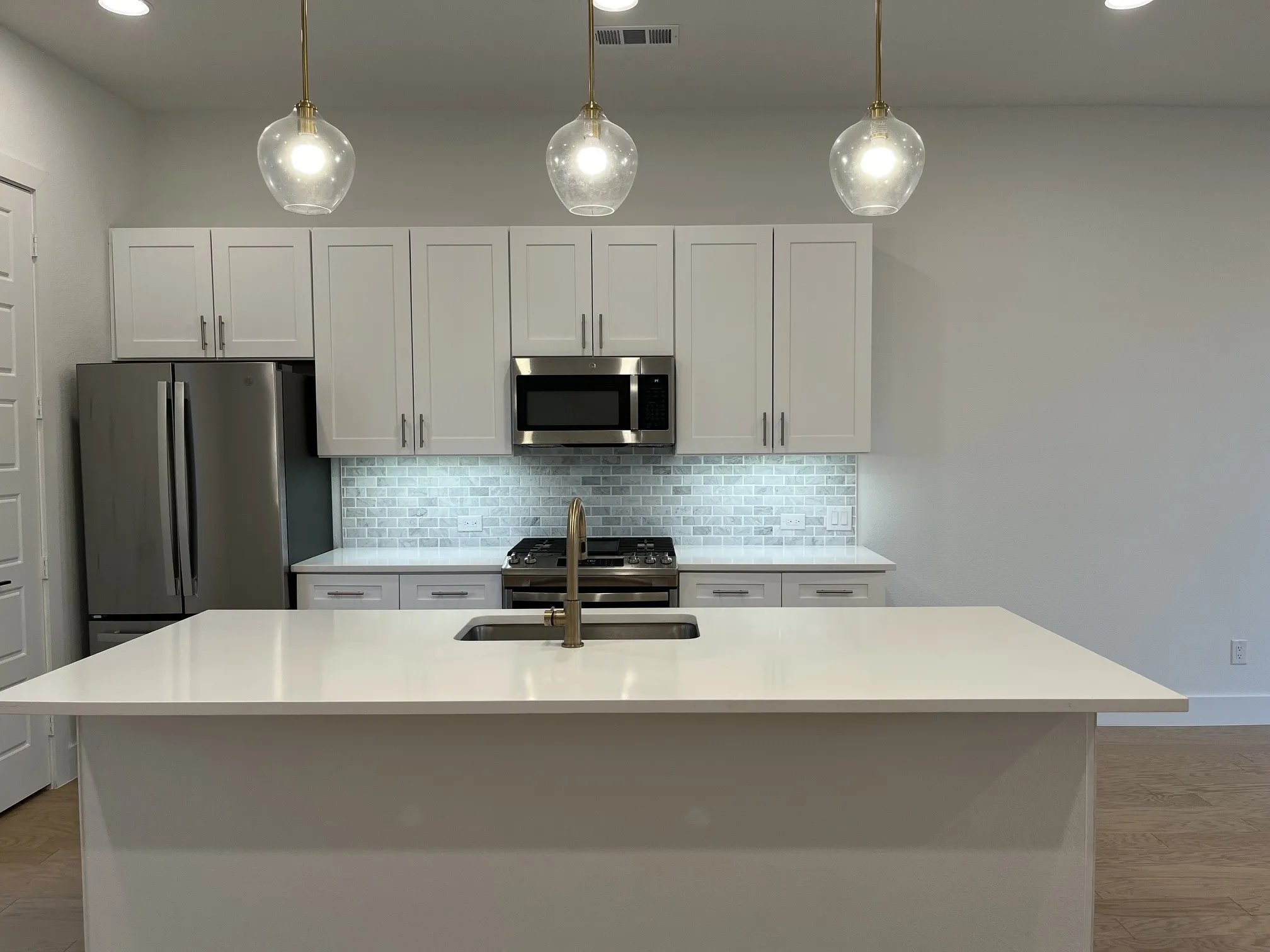 Kitchen with a large island featuring an undermount sink and a brass-finish faucet. Beautiful pendant lighting over kitchen Island.