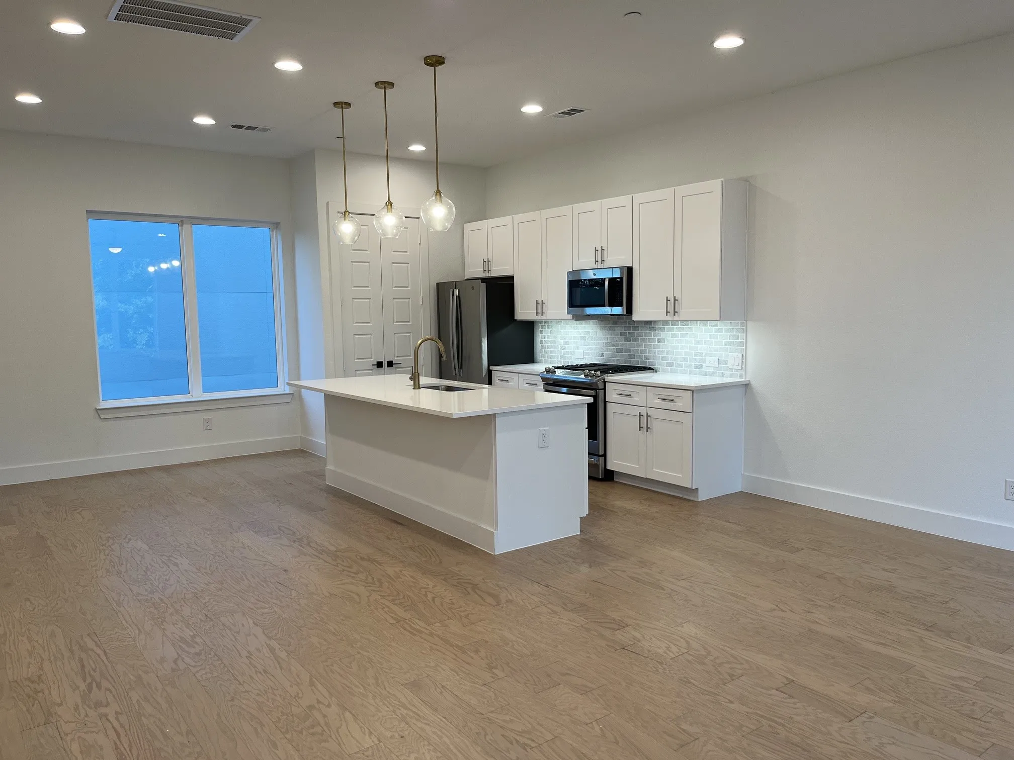 Dining or Kitchen island with a stainless steel faucet, recessed lighting, wood-finish flooring, white cabinetry, and a subway tile backsplash
