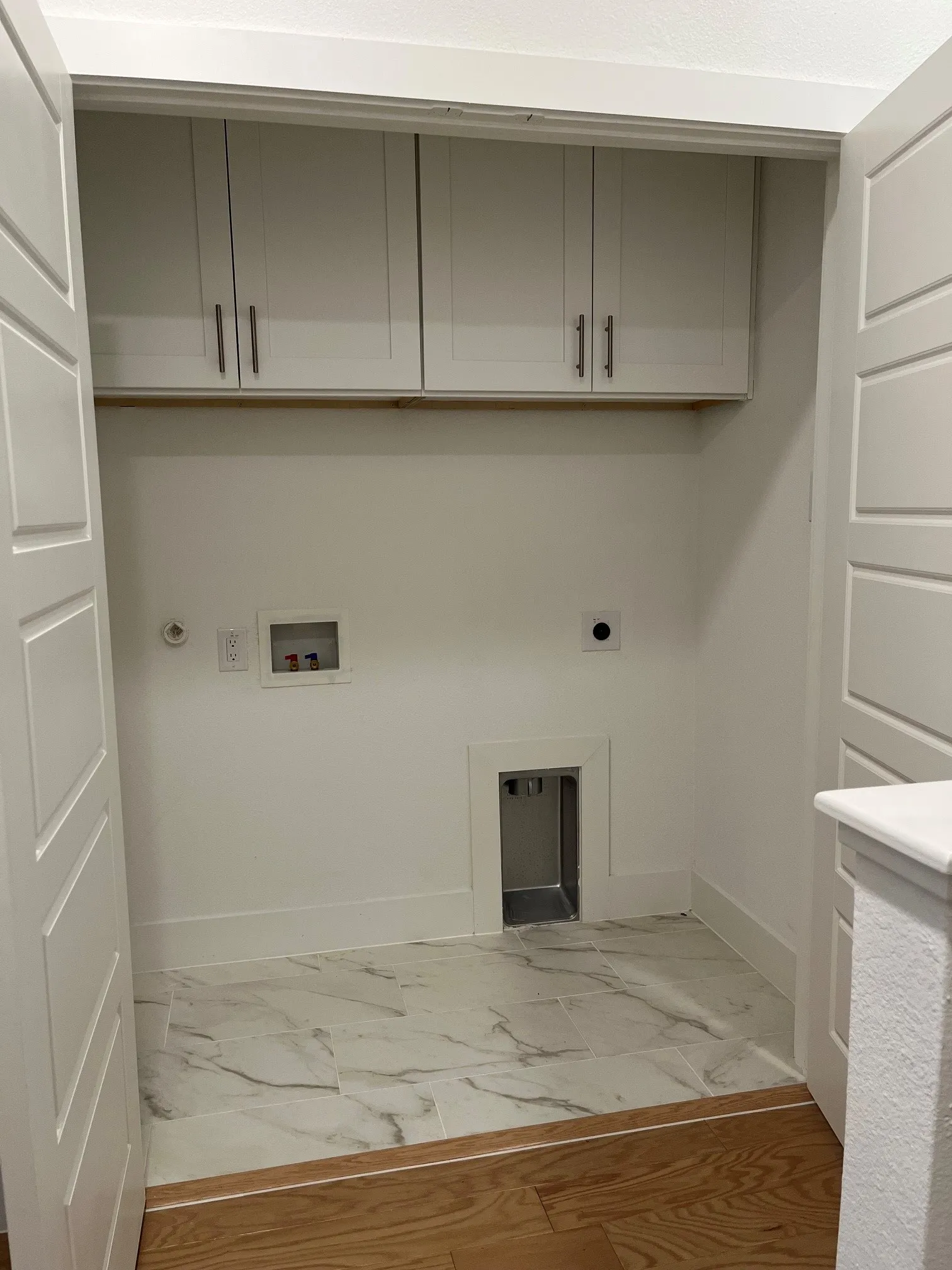 White shaker-style cabinetry with matte black hardware, white tile flooring, and a dedicated utility area
