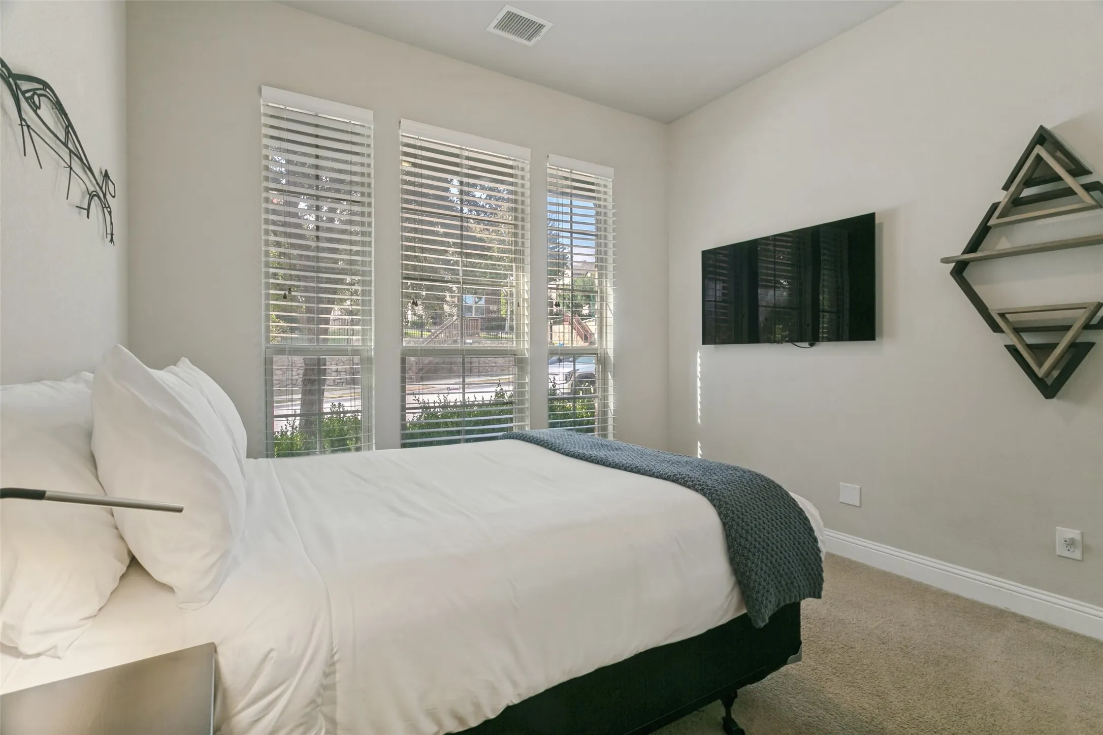 Recessed lighting, three large windows with blinds, wall-mounted display, and neutral carpeting