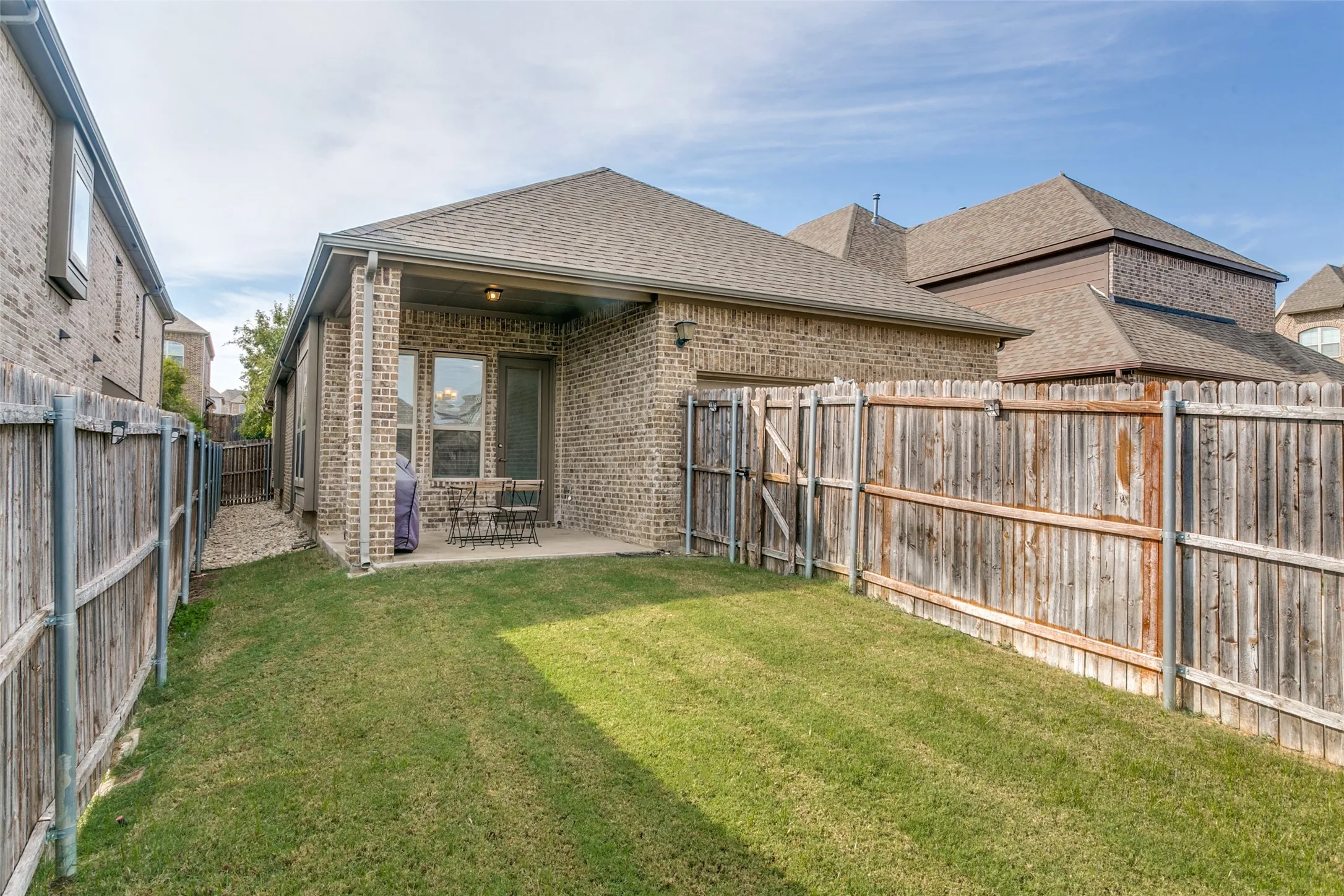 Expansive backyard with a covered patio, brick exterior, and a wood privacy fence