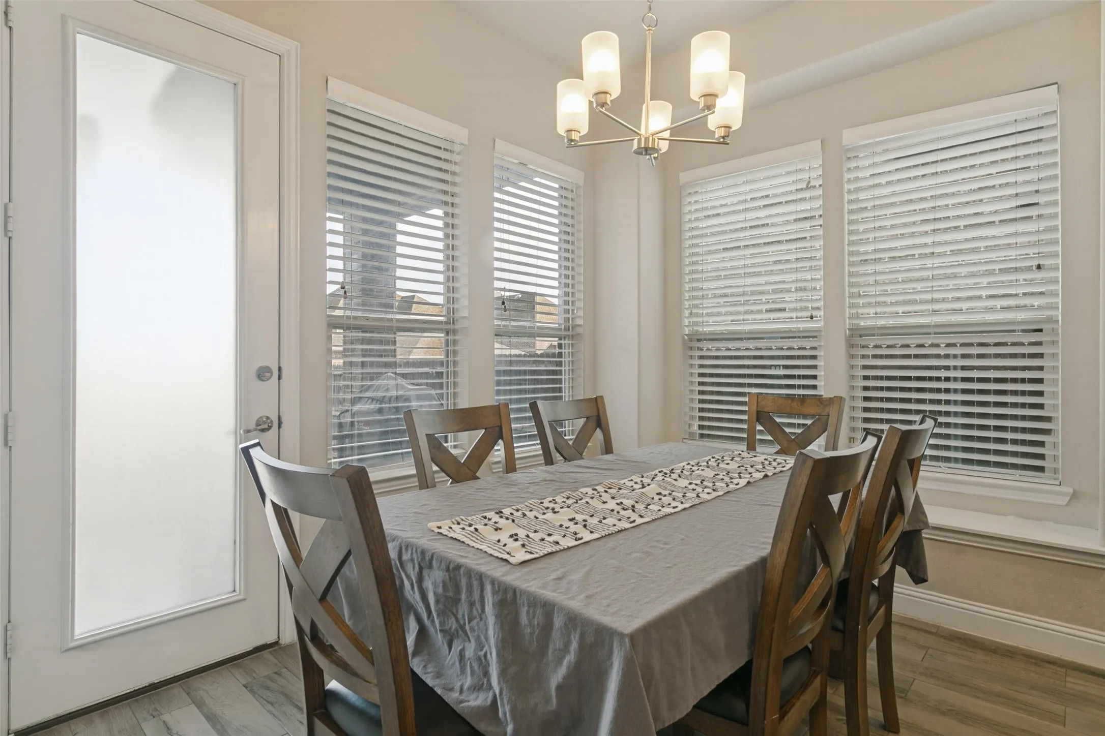 Recessed lighting, wood-finish flooring, multiple windows, frosted glass door, and a multi-light chandelier