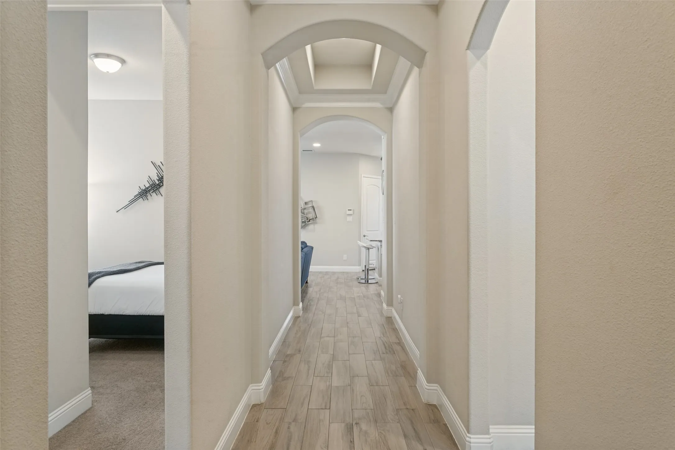 Hallway featuring archways, wood-finish flooring, a coffered ceiling, and neutral wall tones