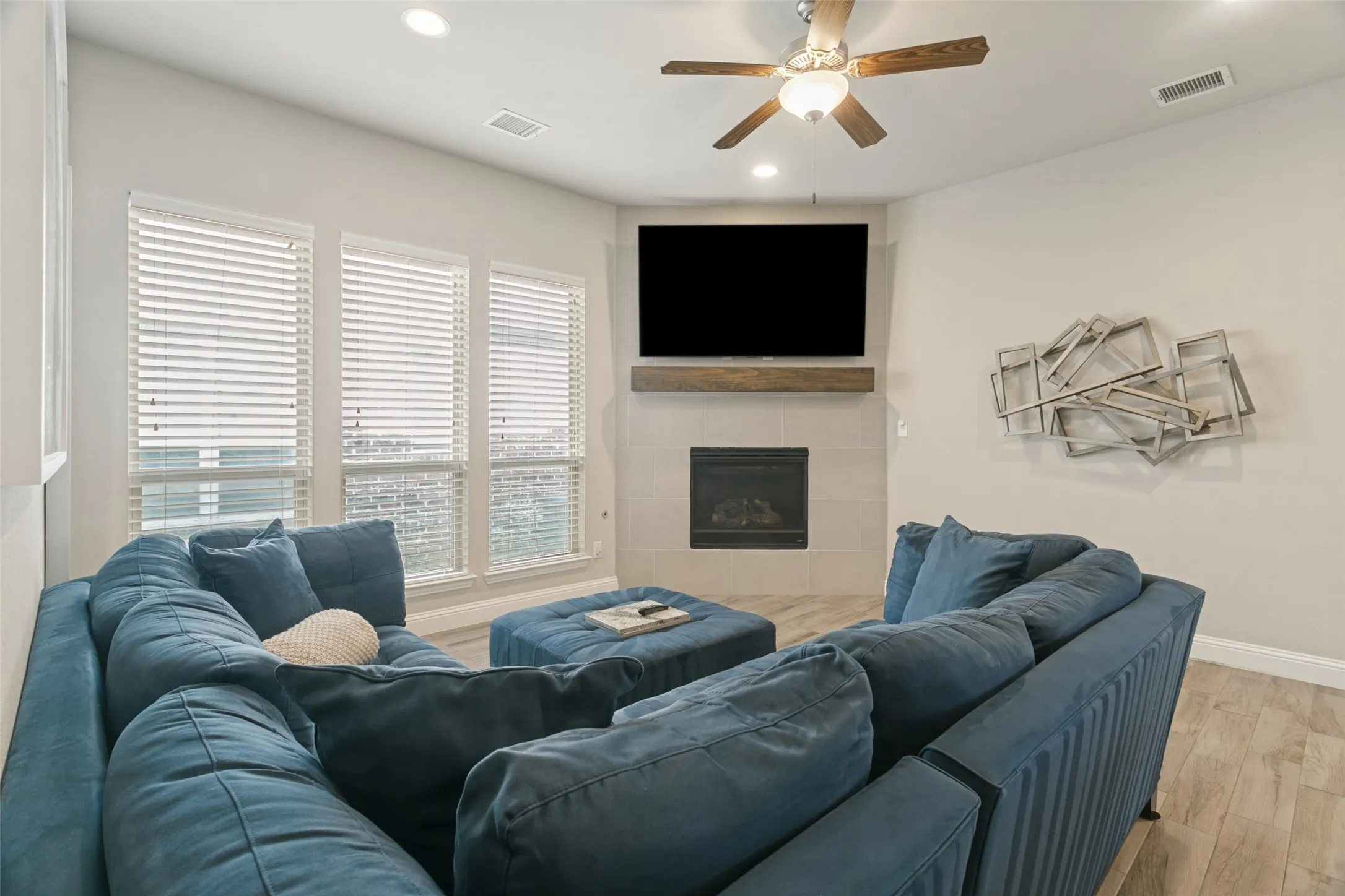 Corner fireplace with a wood mantel, ceiling fan, recessed lighting, and wood-finish flooring