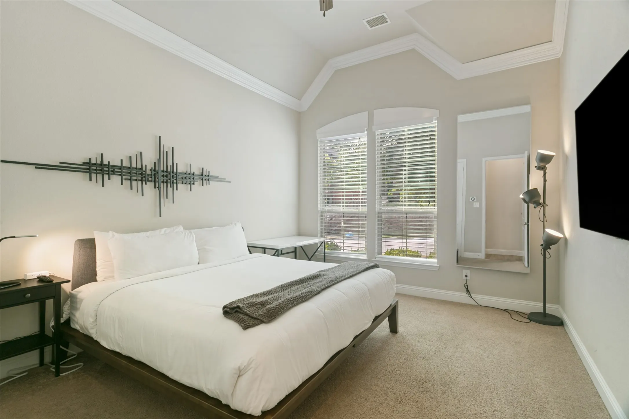 Vaulted ceiling with crown molding, arched windows, light-toned wall paint, and carpeting