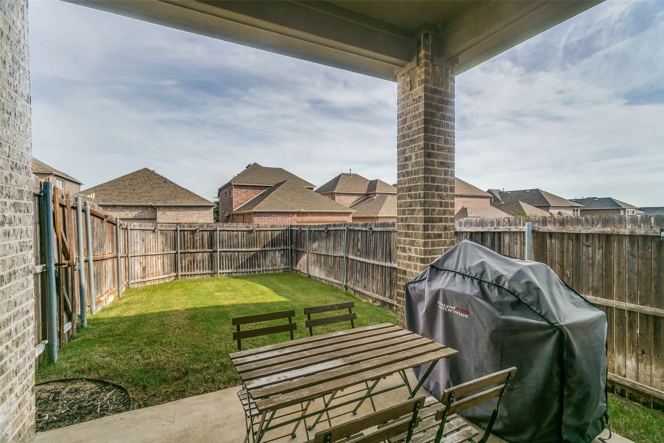 Covered patio with brick column, concrete flooring, and a fenced yard with grass