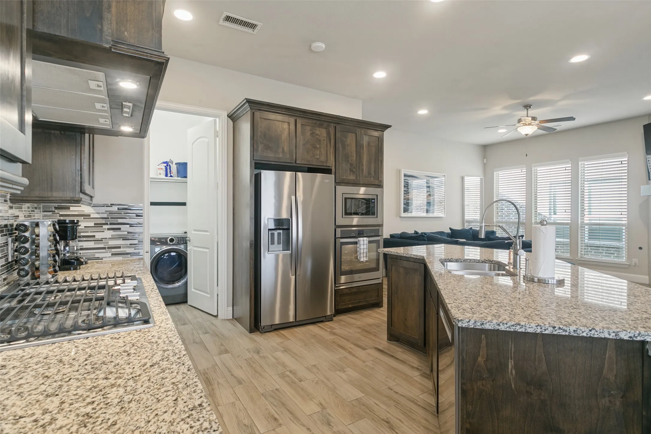 Kitchen featuring granite countertops, wood-finish flooring, stainless steel appliances, and dark wood cabinetry