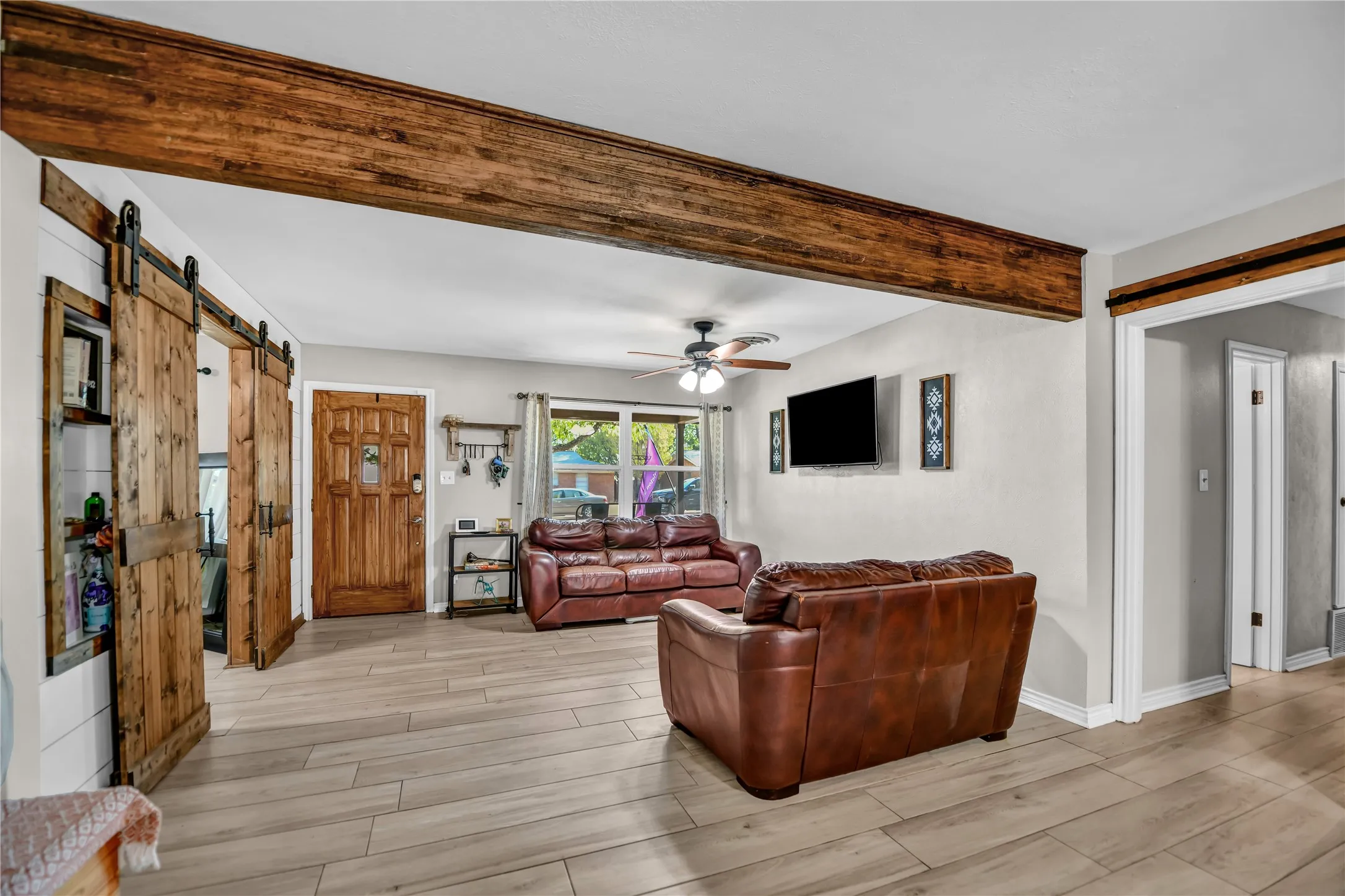 Wood-finish flooring throughout, exposed wood beam ceiling detail, wood barn doors, wood entry door, and a ceiling fan