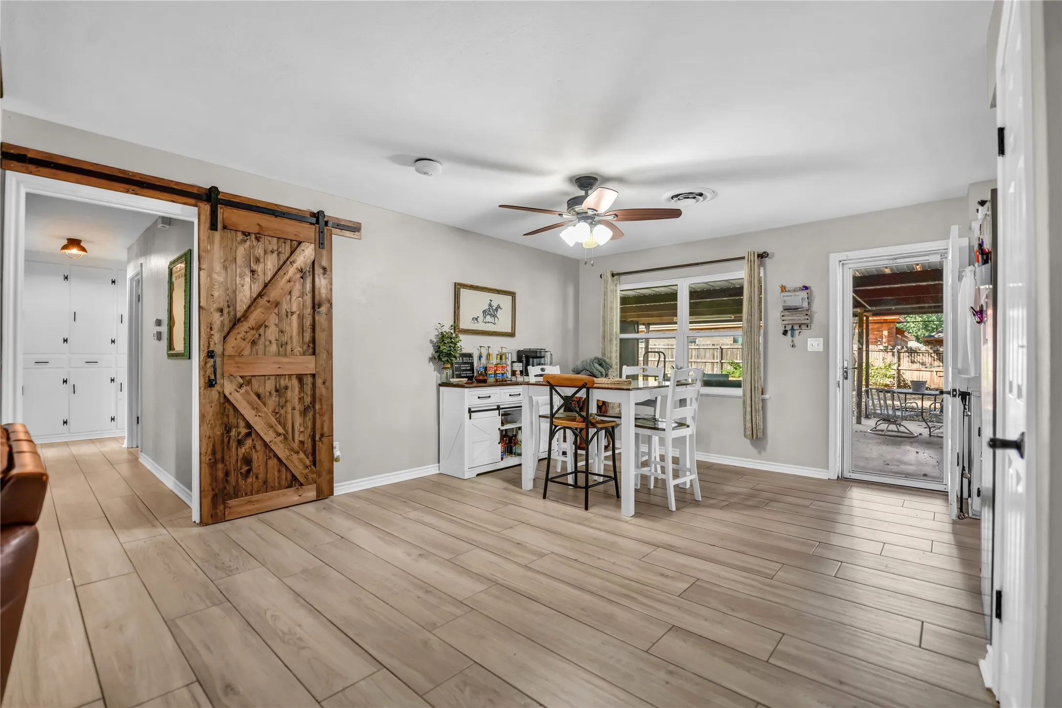 Wood-finish flooring, a ceiling fan with integrated lighting, a natural wood barn door, and a glass-paneled exterior door