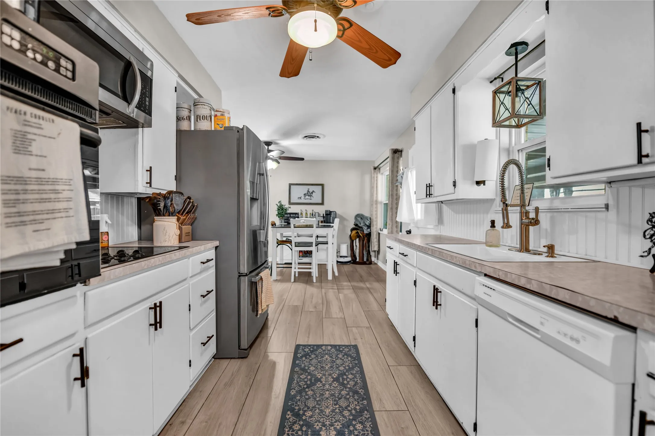 Galley kitchen featuring white cabinetry, modern black hardware, light-toned countertops, and wood-finish flooring