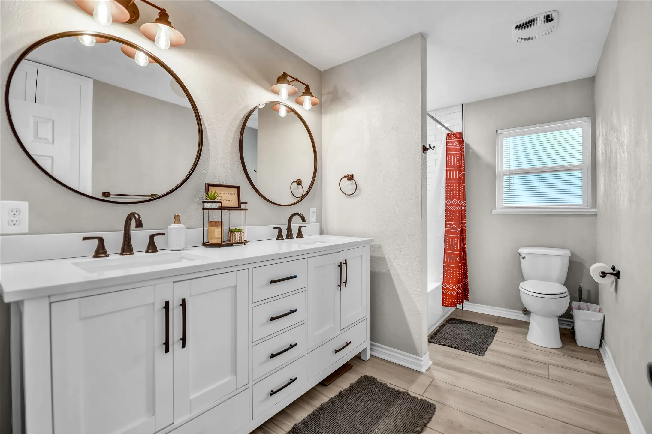 Double vanity with white cabinetry, bronze hardware, and two circular mirrors