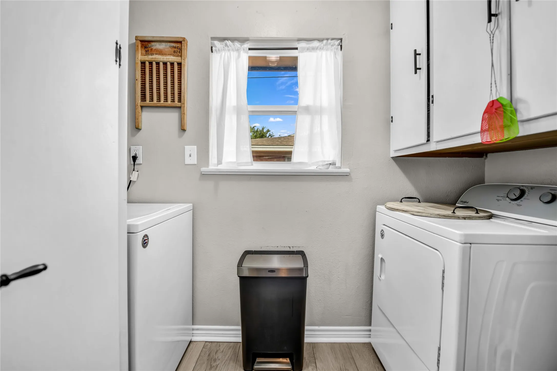 Window with natural light, wood-finish flooring, overhead cabinetry, and light-toned walls