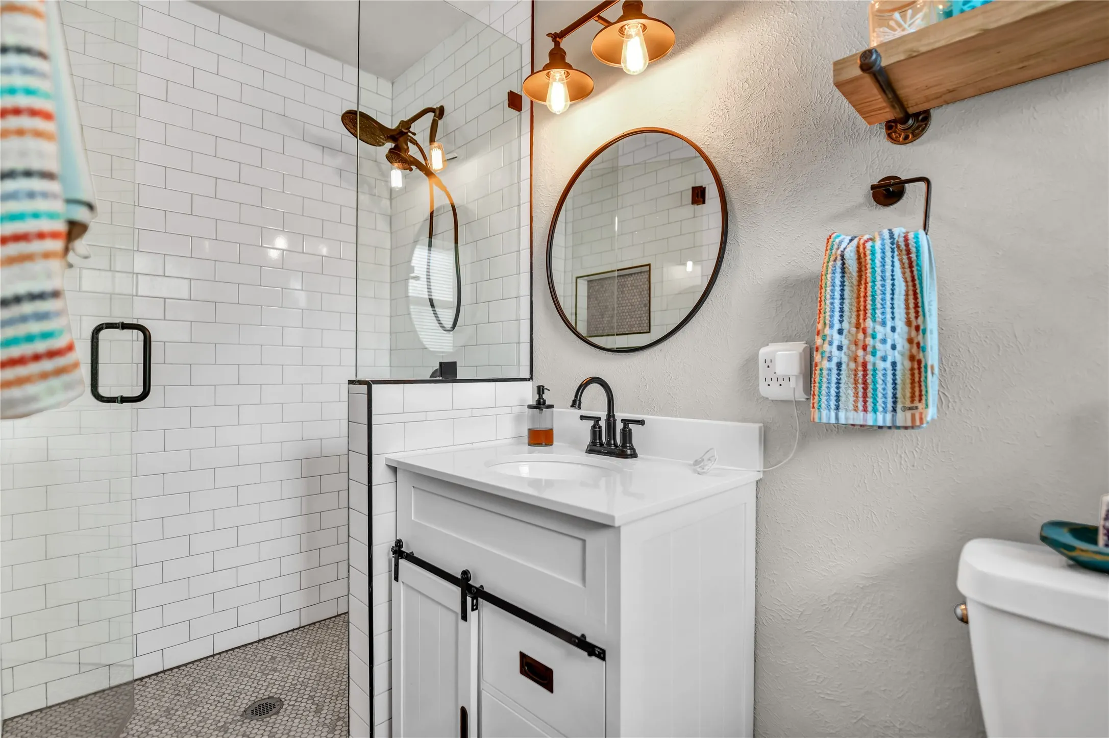 Glass-enclosed shower with white subway tile and mosaic floor