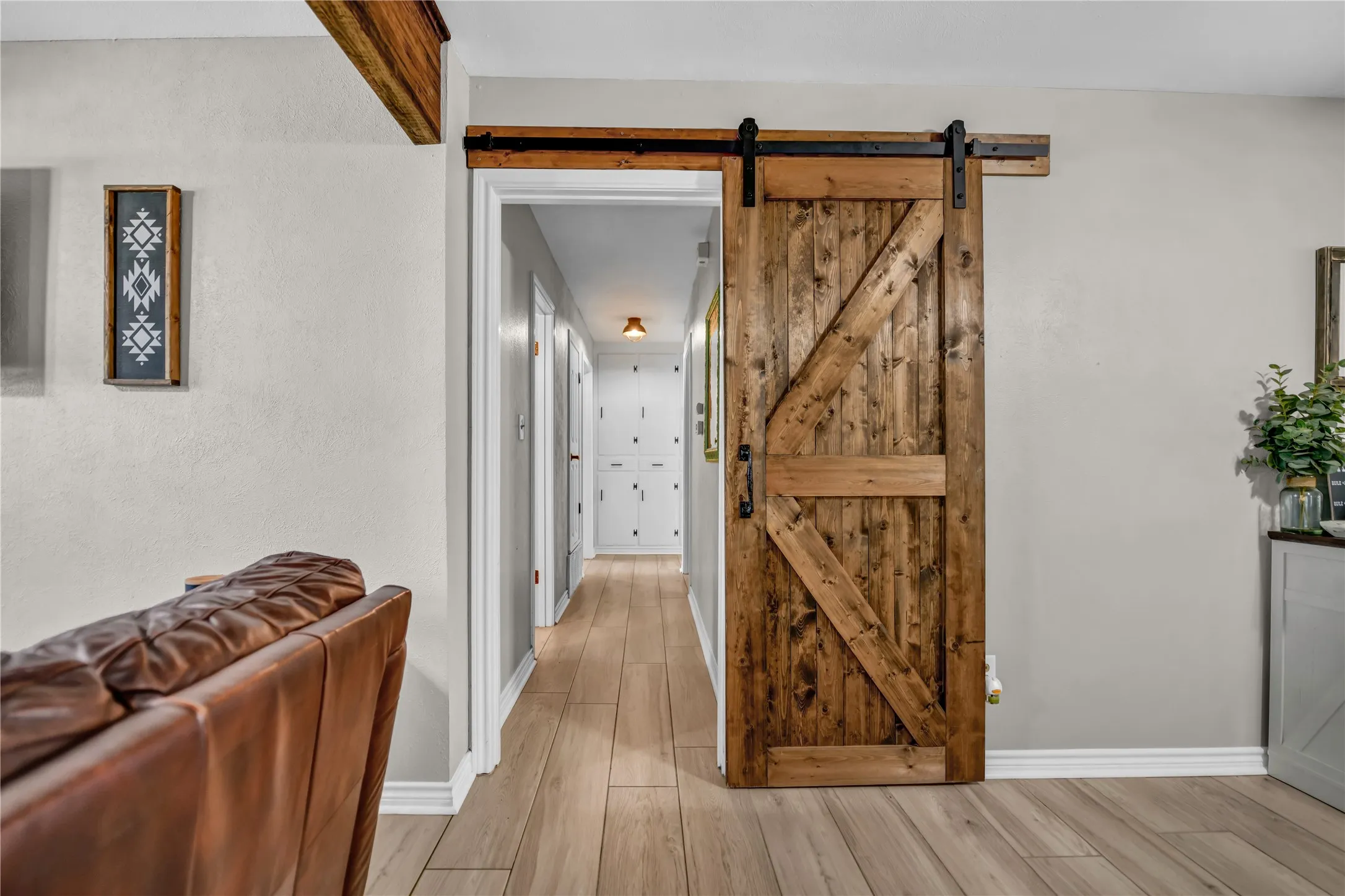 Wood-finish flooring throughout, complemented by a rustic wood barn door with black hardware, and a wood beam ceiling accent