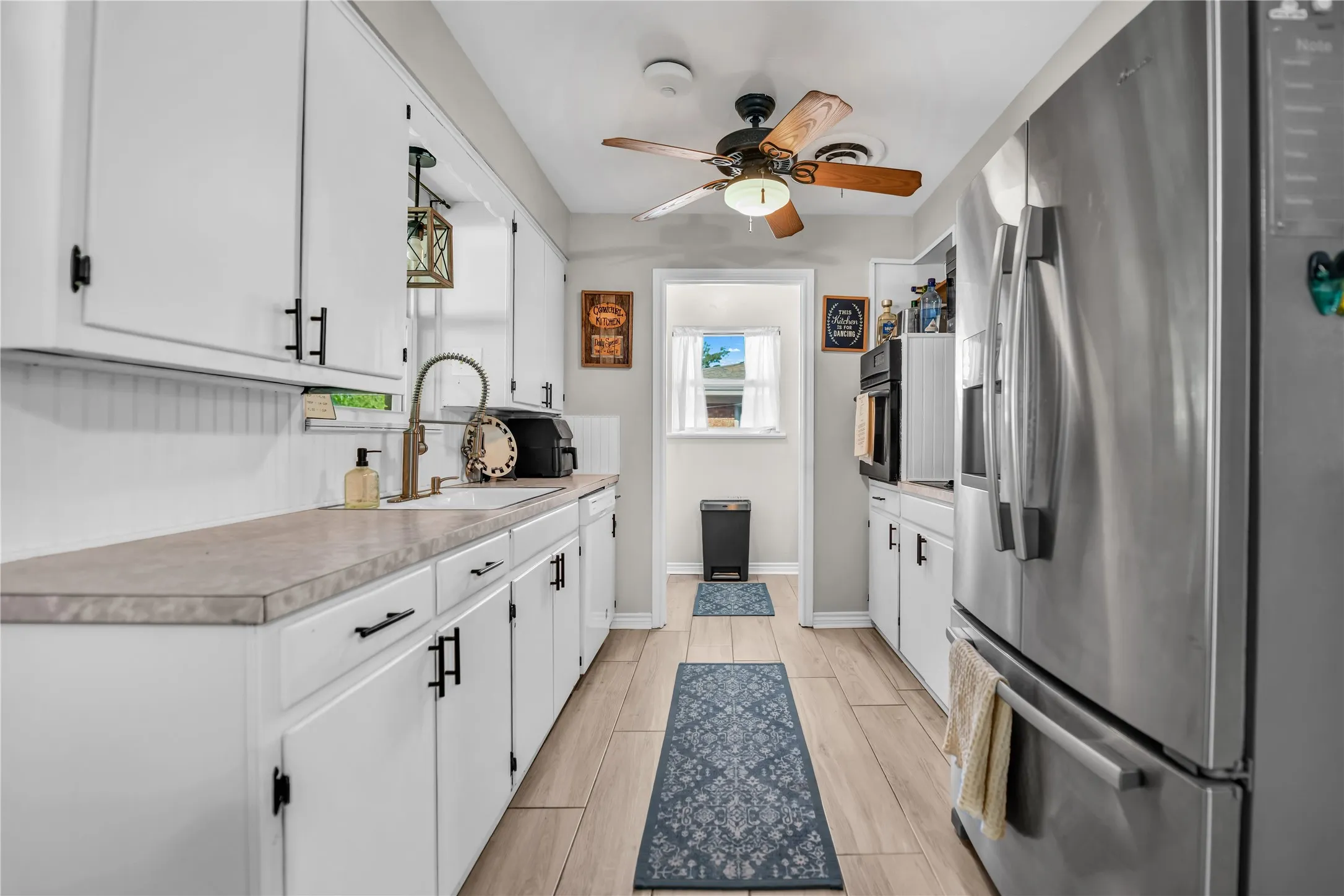 Galley kitchen featuring wood-finish flooring, white cabinetry with matte black hardware, stainless steel appliances, and a ceiling fan