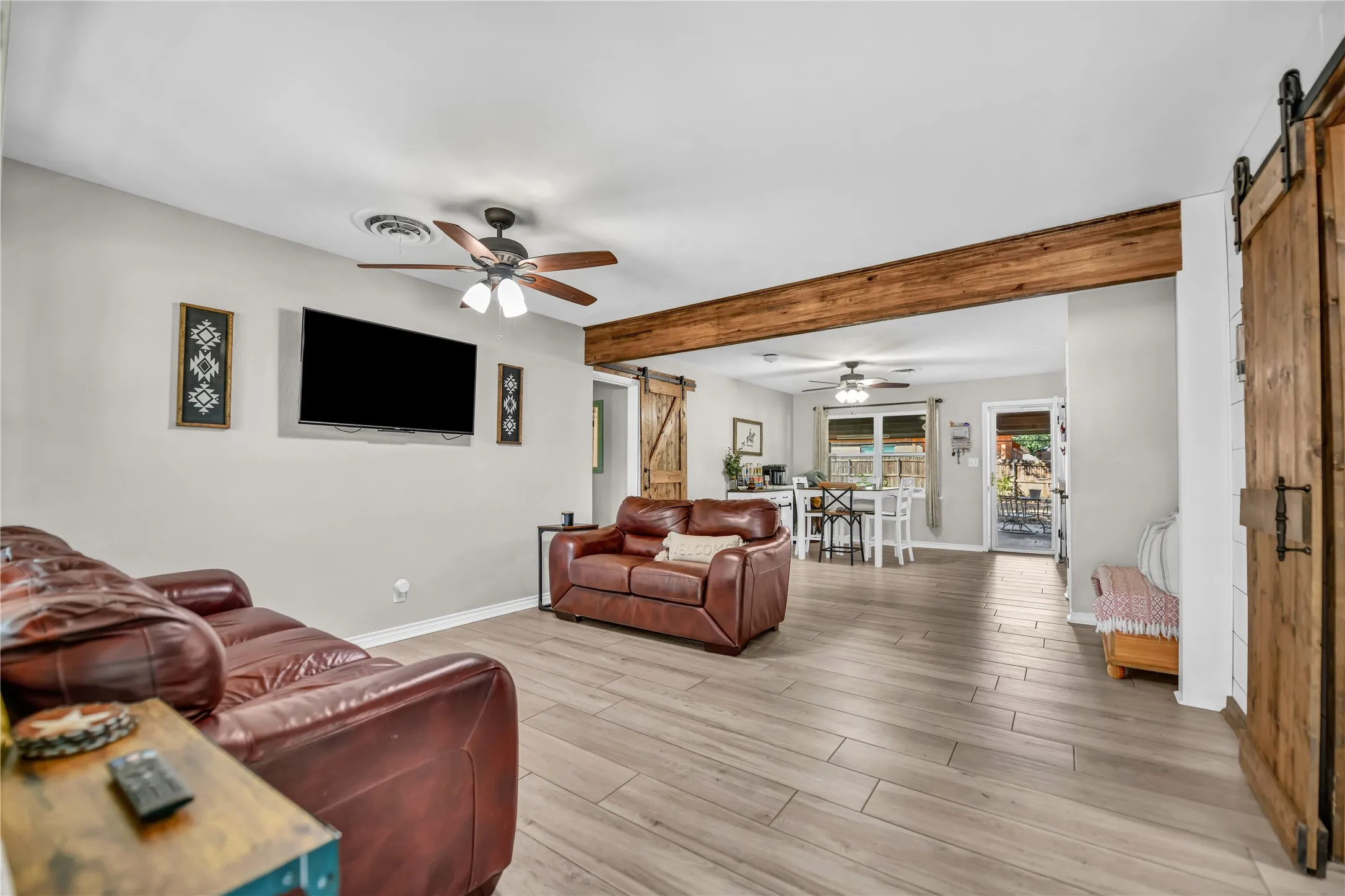 Living area featuring wood-finish flooring, a ceiling fan with integrated lighting, and an exposed wood beam
