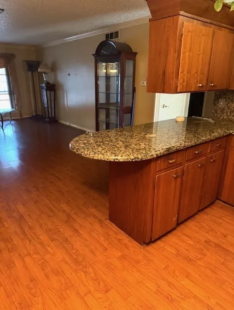 Wood-finish flooring throughout, complemented by a kitchen island with a stone countertop and wood cabinetry