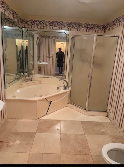 Corner soaking tub, enclosed shower with frosted glass, wall-mounted mirrors, pedestal sink, and tiled flooring