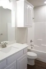 White vanity with integrated sink, brushed nickel faucet, wall-mounted upper cabinet, white toilet, and tub with shower