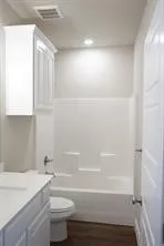 White shaker-style cabinetry with a countertop, white toilet, and a combined tub and shower unit