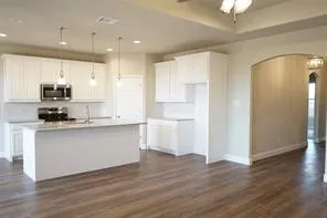 Open-concept kitchen featuring white cabinetry, stainless steel microwave, kitchen island with sink, and wood-finish flooring