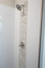 Shower enclosure with white subway tile, mosaic tile accent strip, and a chrome shower head and control