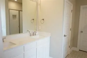 Double vanity with integrated sinks and brushed nickel faucets, featuring white cabinetry, a large wall-mounted mirror, and a shower with a sliding glass door