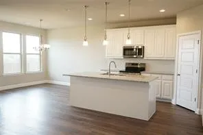 Kitchen island with integrated sink, stainless steel appliances, wood-finish flooring, white cabinetry, and recessed lighting