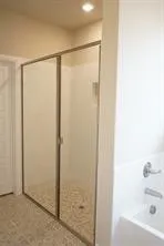 Shower enclosure with clear glass panels, tiled shower floor, and adjacent bathtub with chrome fixtures