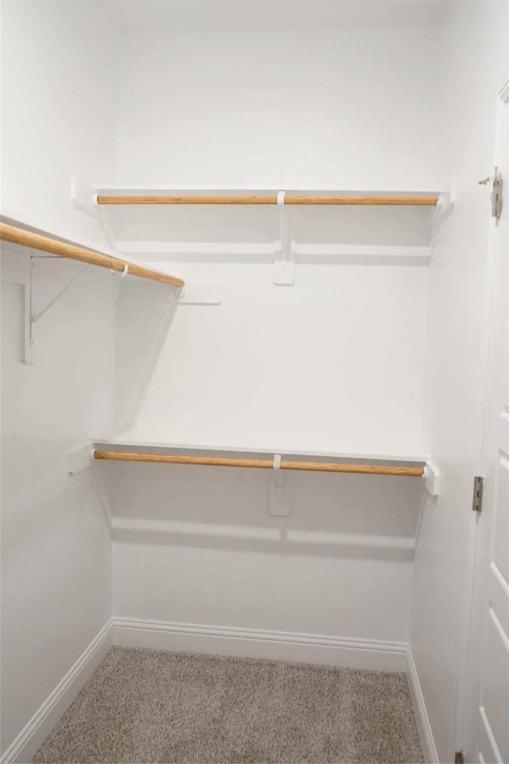Organized closet space featuring multiple wooden hanging rods with white metal brackets, carpet flooring, and ample wall storage for efficient wardrobe arrangement