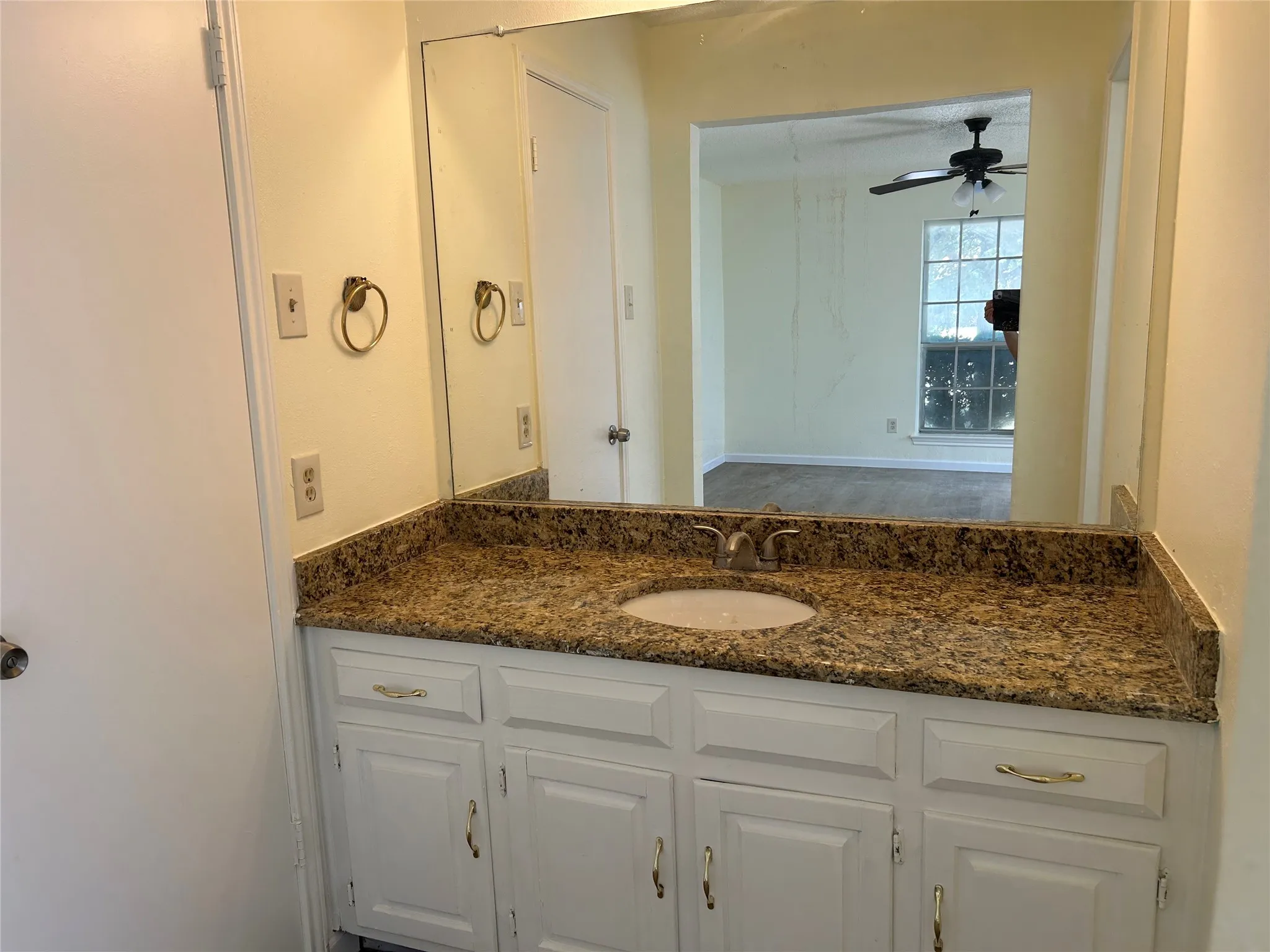 Single vanity with integrated sink, stone-finish countertop, and white cabinetry with gold-tone hardware