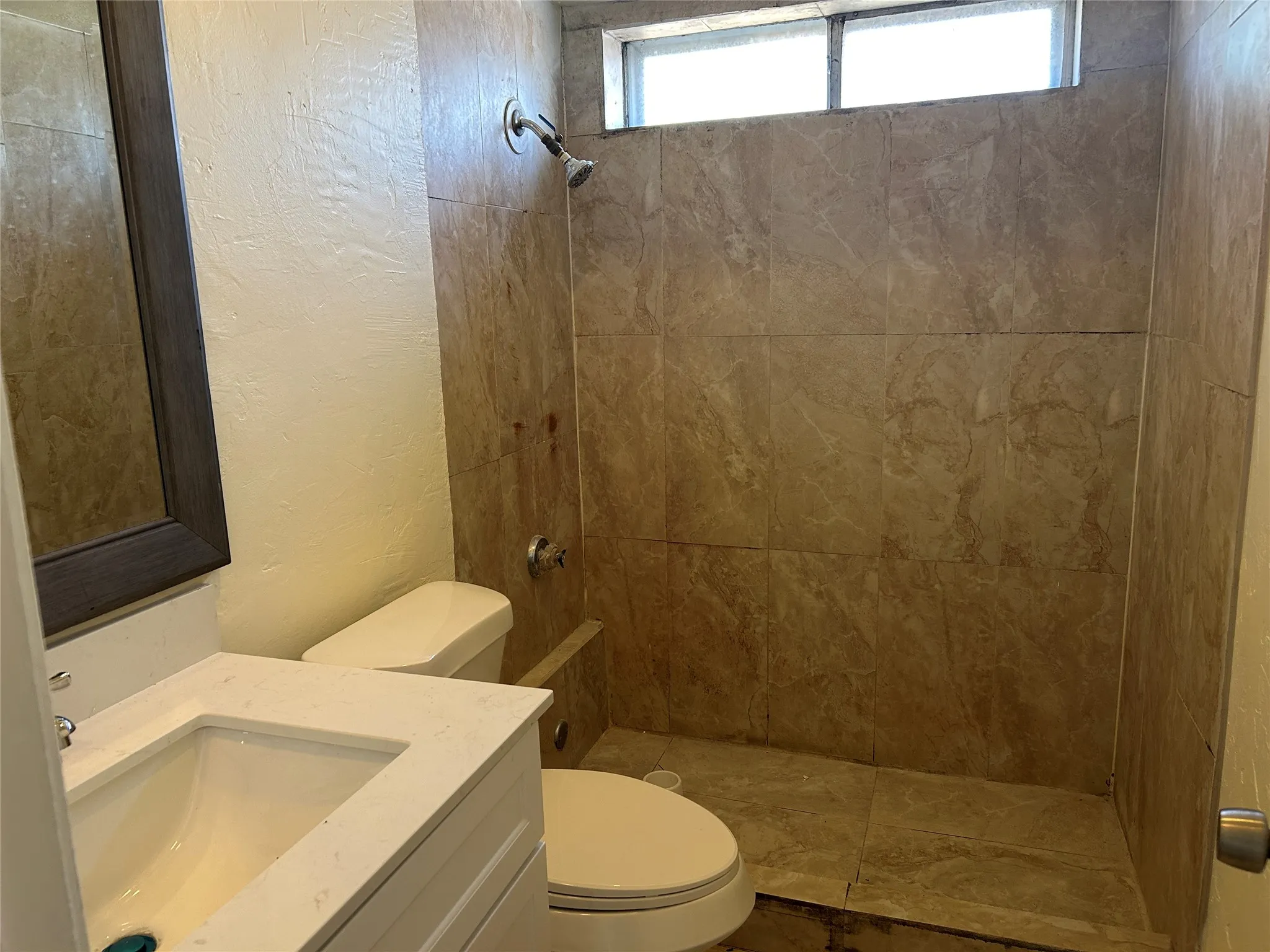 Tiled shower stall with a built-in bench, frosted transom window, and showerhead
