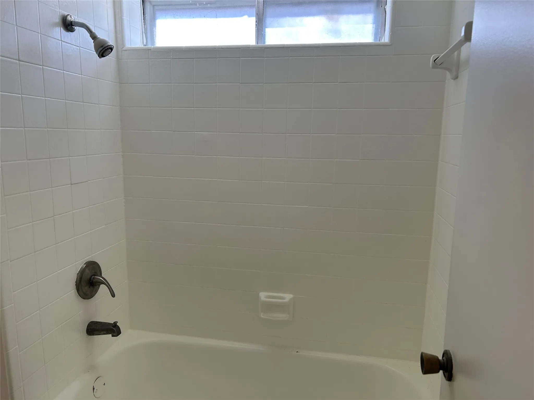 Bathtub and shower combination featuring white tiled surround, window, and a shower curtain rod