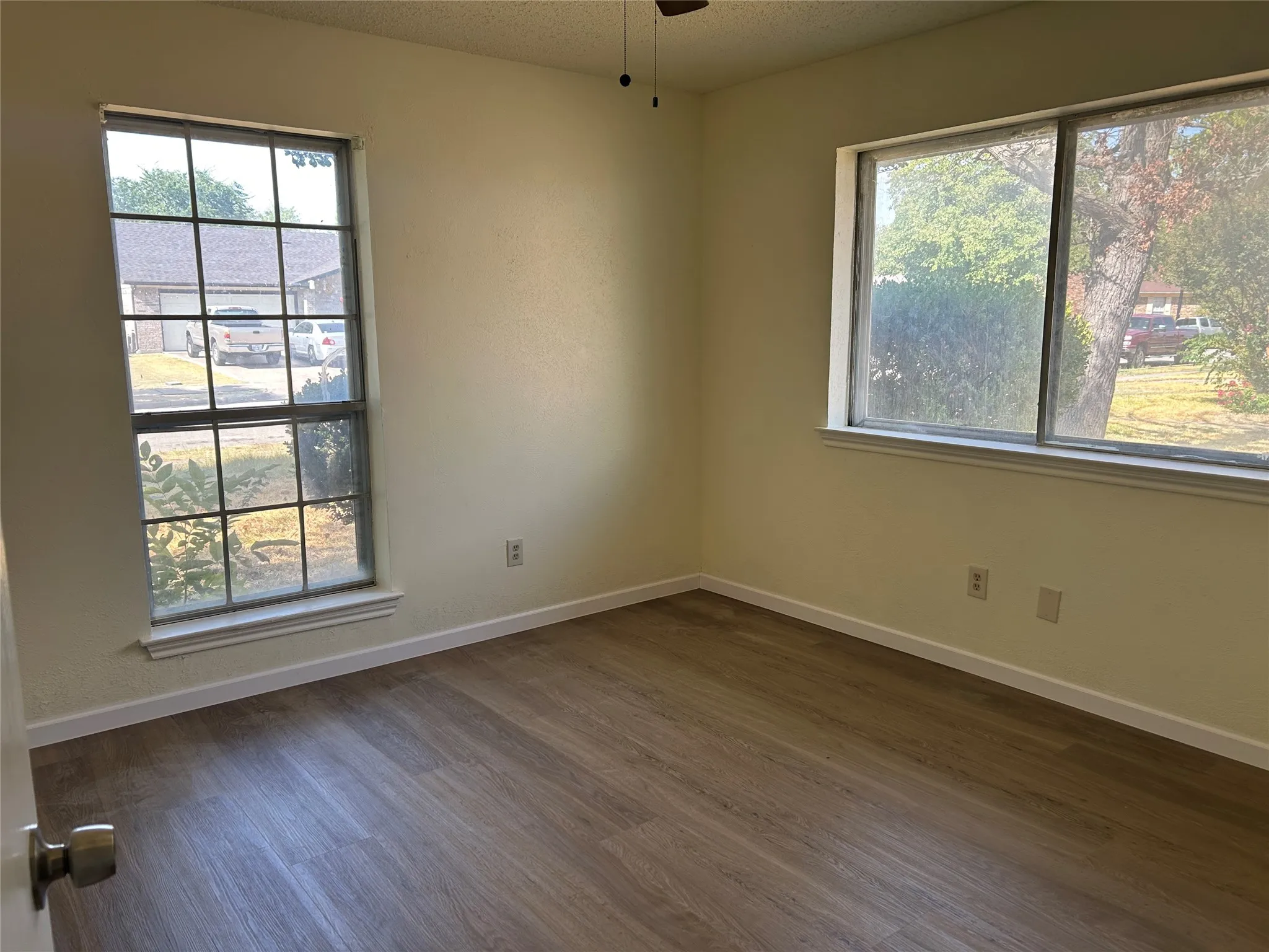 Wood-finish flooring, multiple windows, ceiling fan, and neutral wall paint
