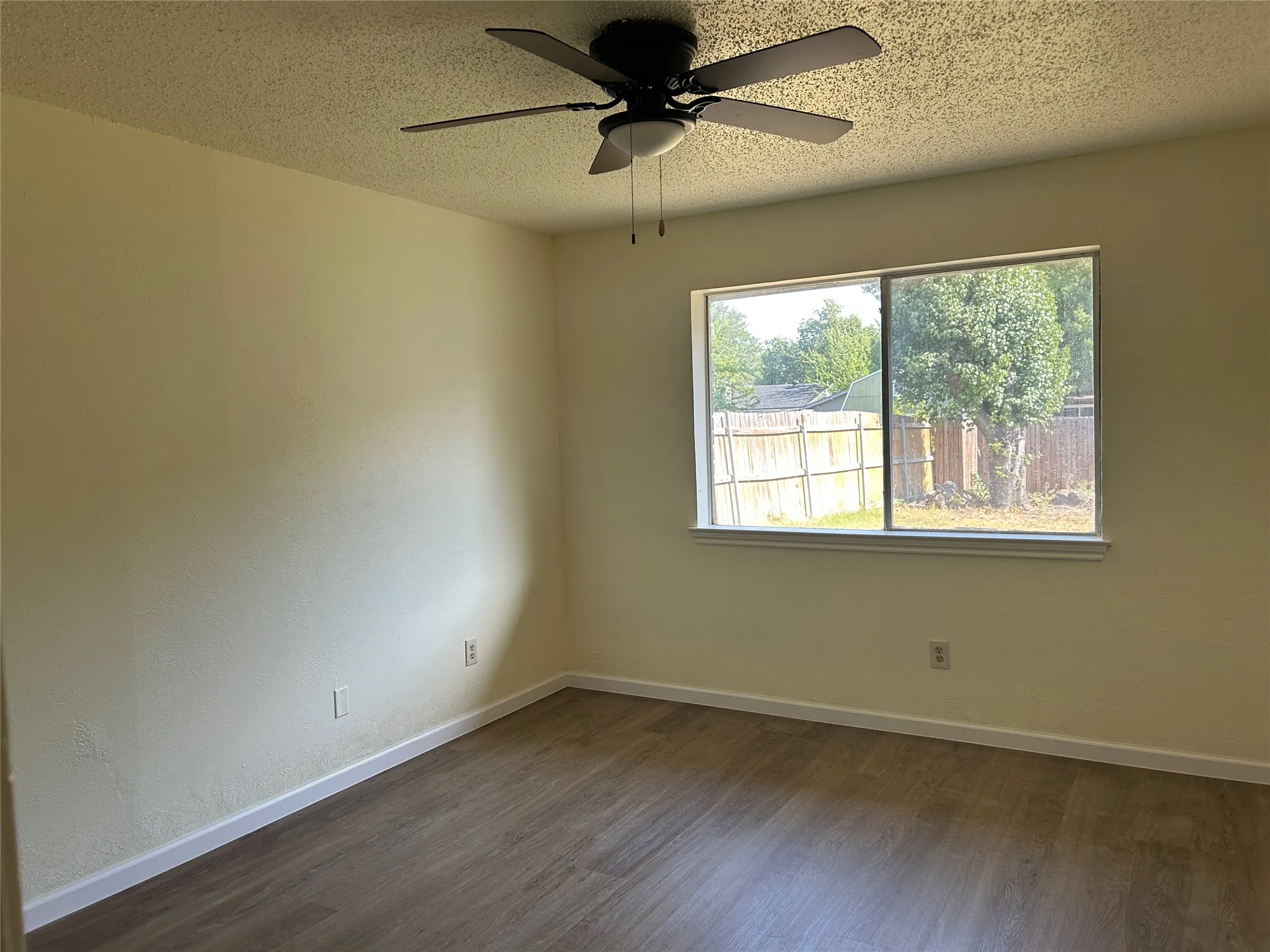 Wood-finish flooring, neutral wall tones, and a window with a fenced perimeter